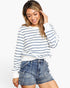 A woman wearing a white long-sleeve crewneck sweatshirt with thin navy blue horizontal stripes, paired with high-waisted blue denim shorts, against a plain white studio background.