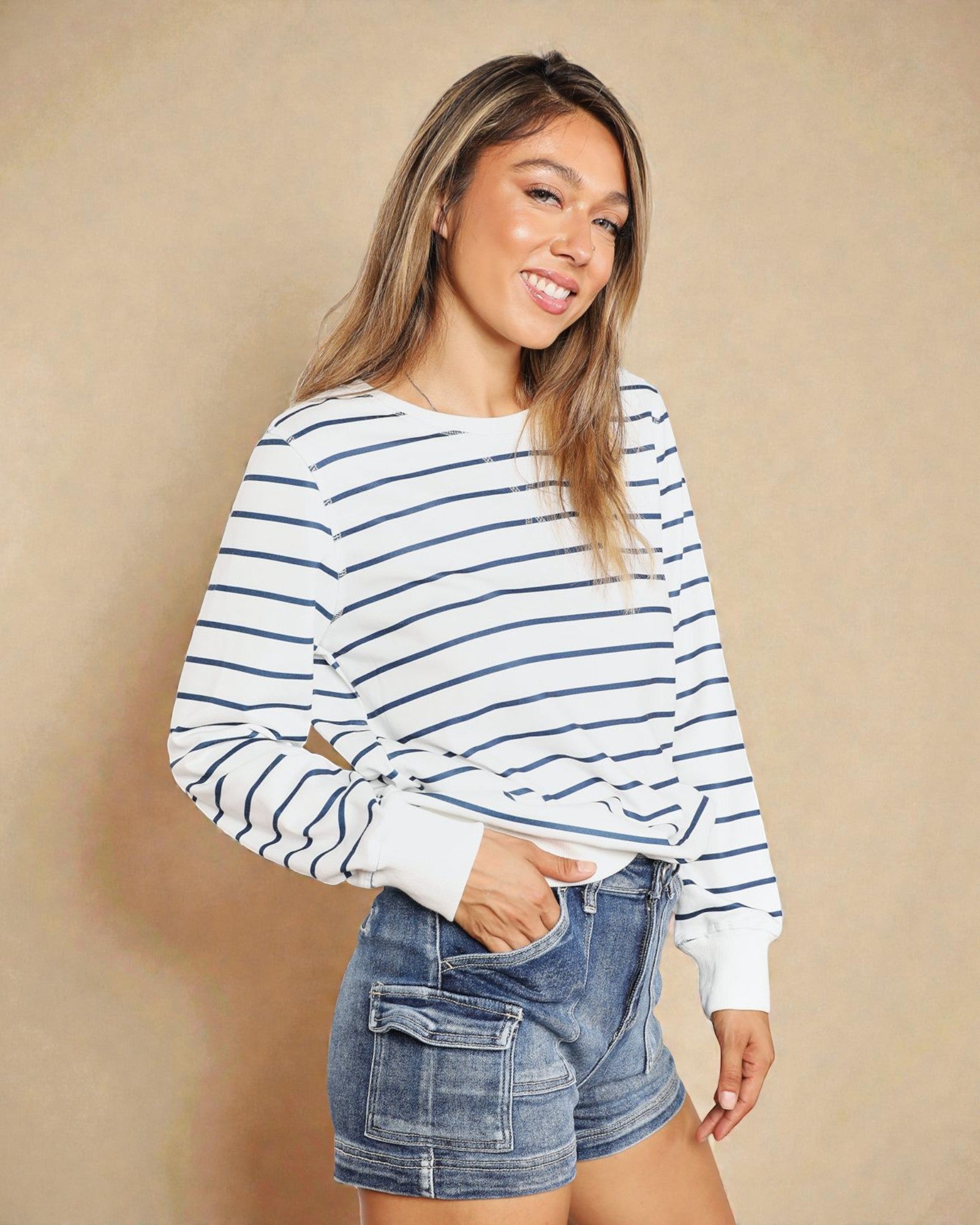 Woman wearing a striped sweater and denim shorts against a beige background
