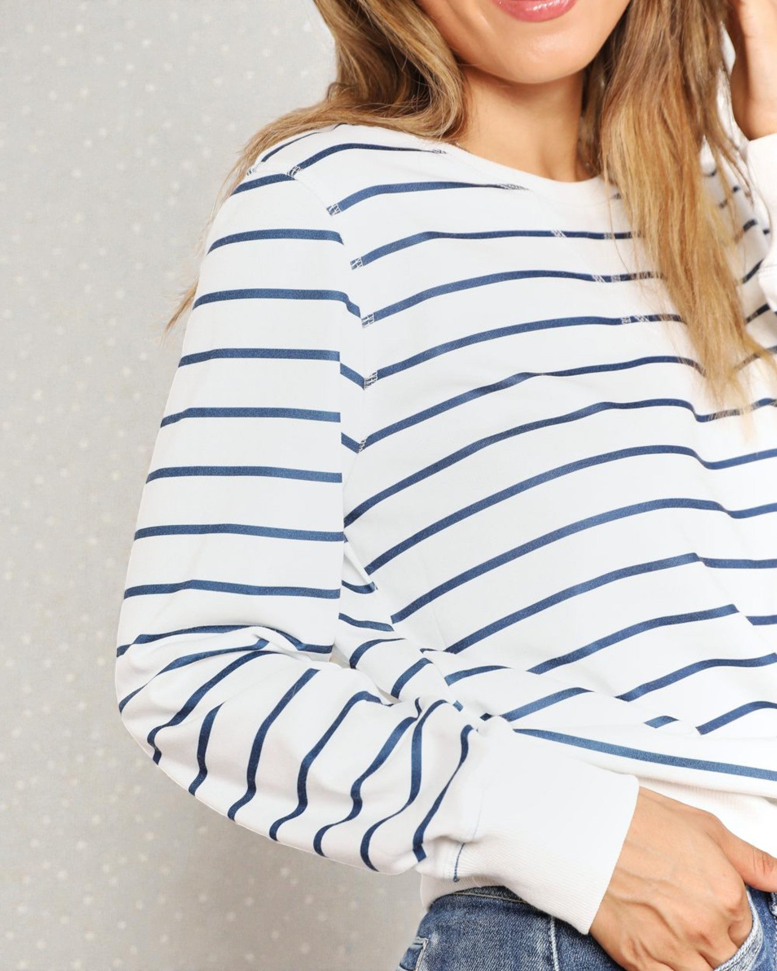 Person wearing a white long-sleeve shirt with blue stripes against a gray background