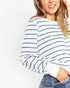 A woman wearing a white long-sleeve crewneck sweatshirt with thin navy blue horizontal stripes, paired with blue jeans, shown against a plain white background.