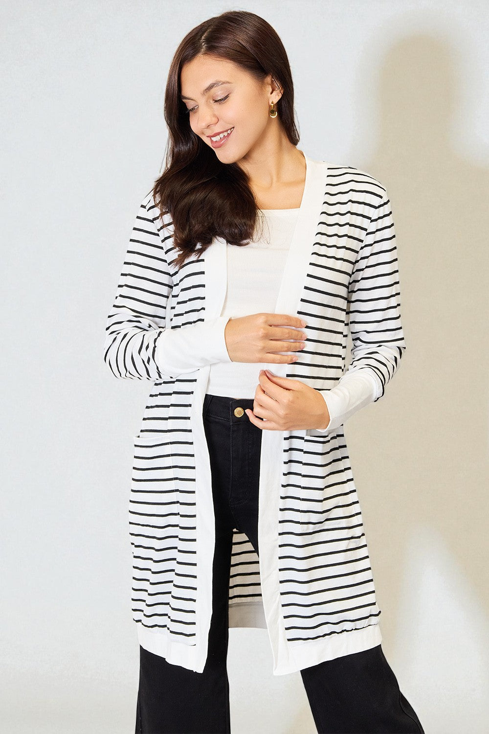 Woman wearing a black and white striped cardigan over a white shirt and black pants on a plain background