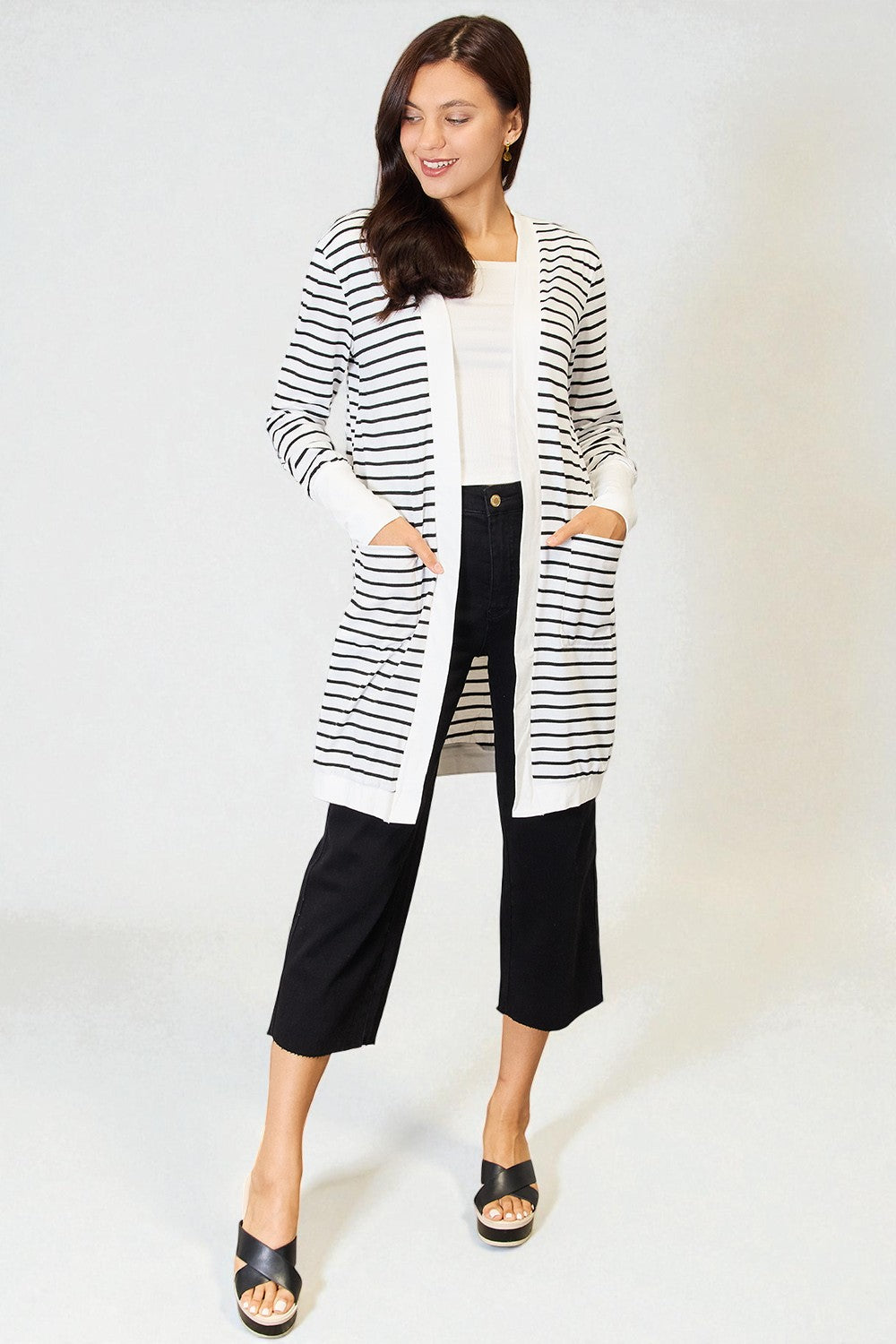 Woman wearing a black and white striped cardigan with black pants on a white background