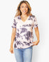 A woman modeling a short-sleeve V-neck tie-dye t-shirt in light pink and dark gray, paired with blue jeans, against a plain white background.