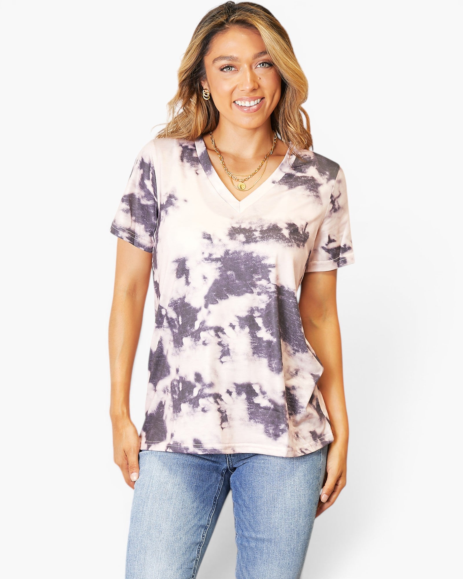A woman modeling a short-sleeve V-neck tie-dye top in light pink and dark purple, paired with blue jeans, against a plain white background.