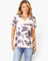 A woman modeling a short-sleeve V-neck tie-dye top in light pink and dark purple, paired with blue jeans, against a plain white background.