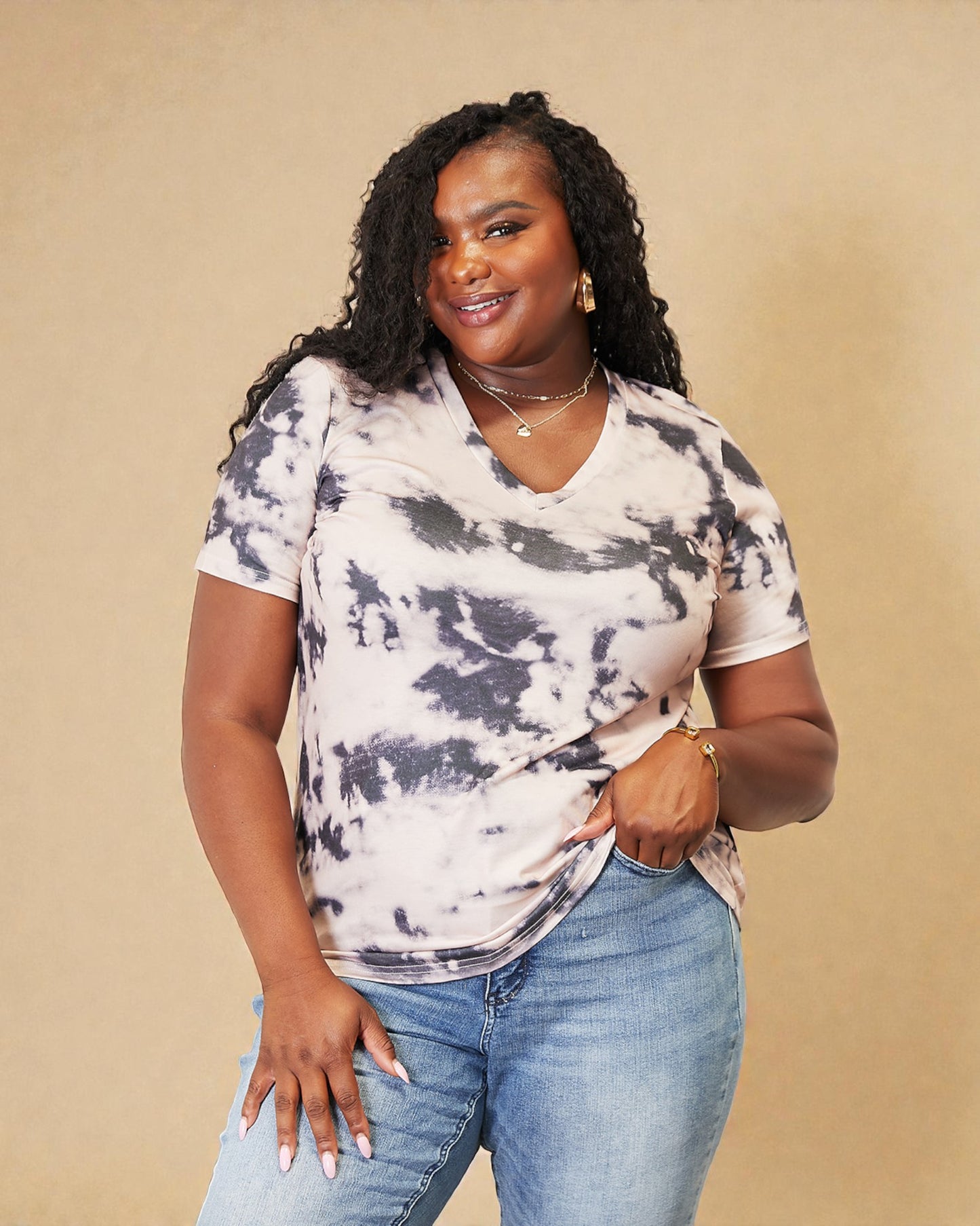 Woman wearing a tie-dye shirt and jeans against a beige background