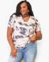 A woman modeling a short-sleeve V-neck tie-dye t-shirt in beige and gray, paired with blue jeans, against a plain white background.