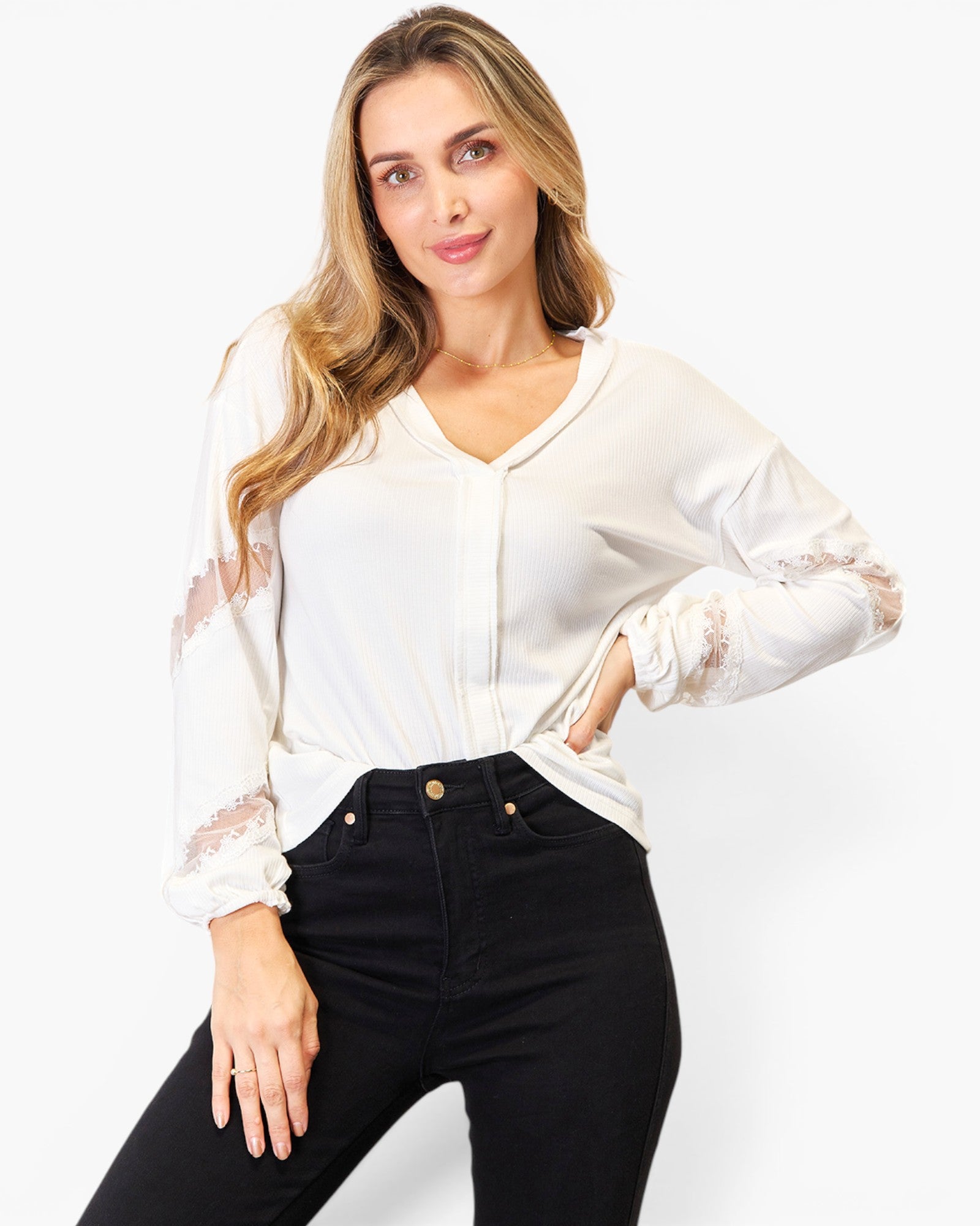 A woman modeling a white long-sleeve blouse with sheer lace cuffs and black jeans against a plain white studio background.