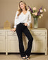 Woman in a white blouse and black pants standing next to a decorative cabinet with flowers.
