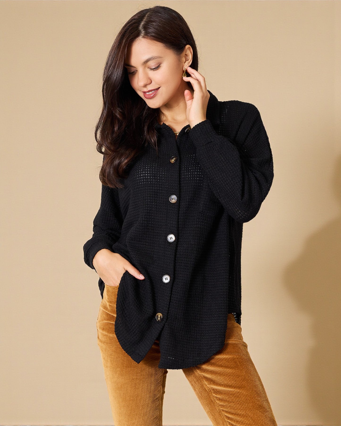 Woman wearing a black textured cardigan over a mustard yellow top against a beige background