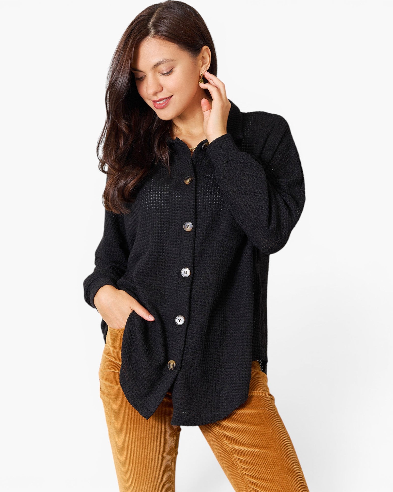 A woman wearing a black textured button-up shirt with brown corduroy pants, posing against a plain white studio background.