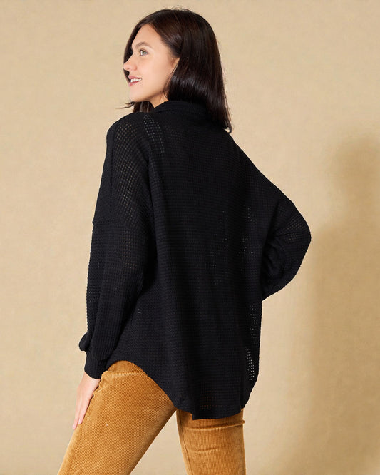Woman wearing a black sweater and brown pants against a beige background