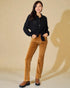 Woman wearing a black sweater and brown velvet pants against a beige background