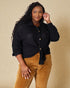 Woman wearing a black textured shirt and brown pants against a beige background