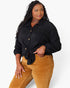 A woman modeling a black textured long-sleeve button-up shirt tied at the waist, paired with mustard corduroy pants, against a plain white studio background.