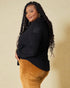 Woman wearing a black top and brown pants against a beige background