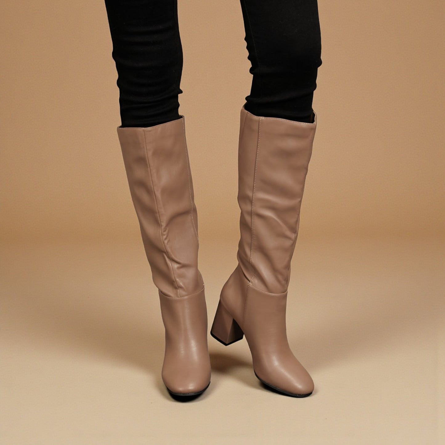 Tan knee-high boots worn with black pants on a beige background