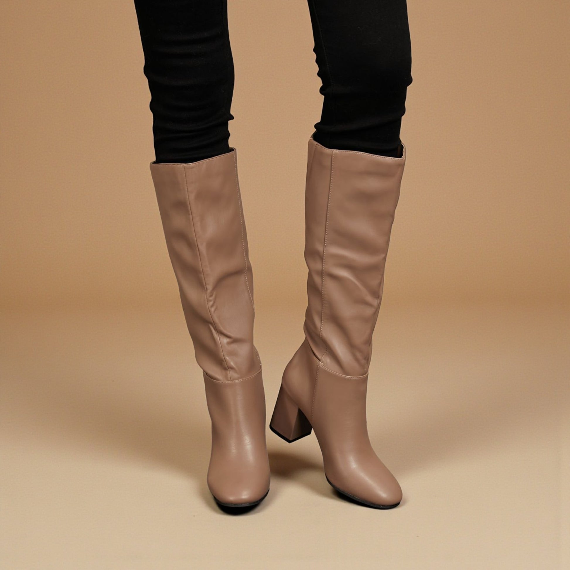 Tan knee-high boots worn with black pants on a beige background