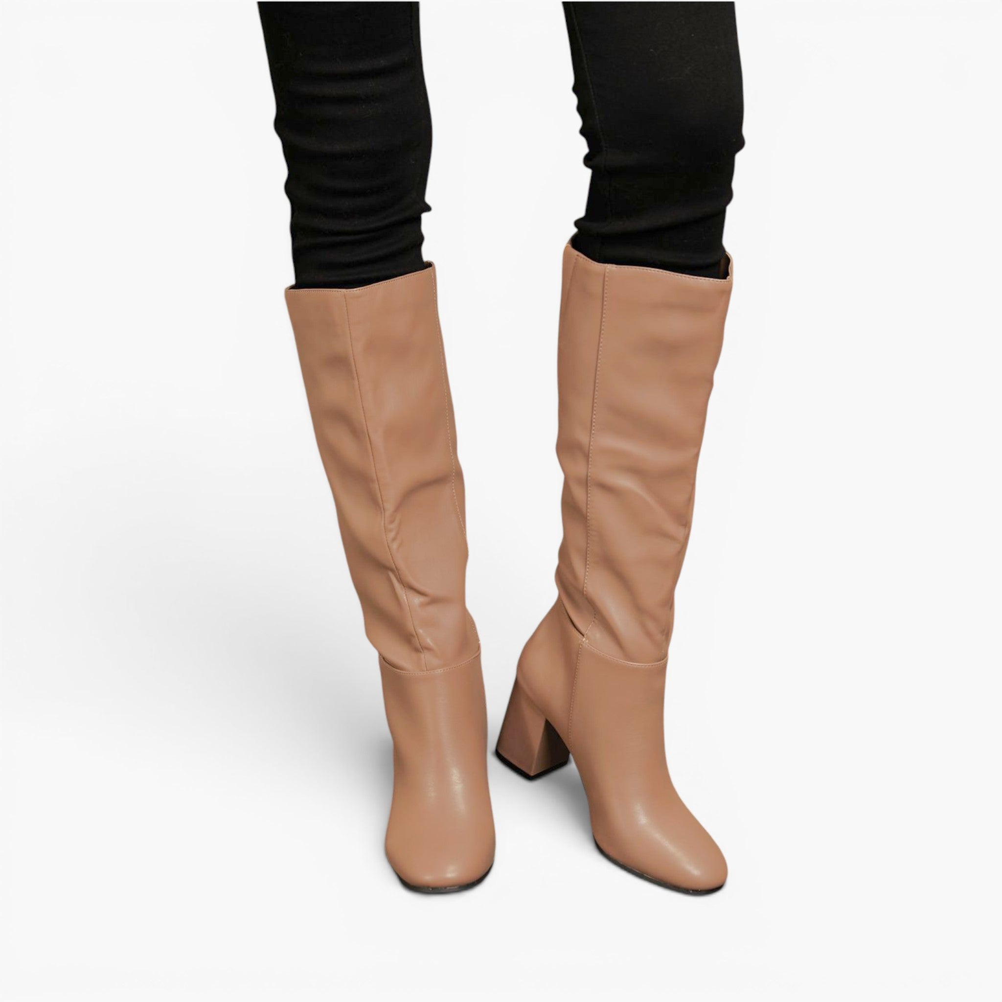 A pair of knee-high tan boots with a block heel, shown on a model wearing black skinny pants against a plain white background.