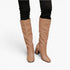 A pair of knee-high tan boots with a block heel, shown on a model wearing black skinny pants against a plain white background.