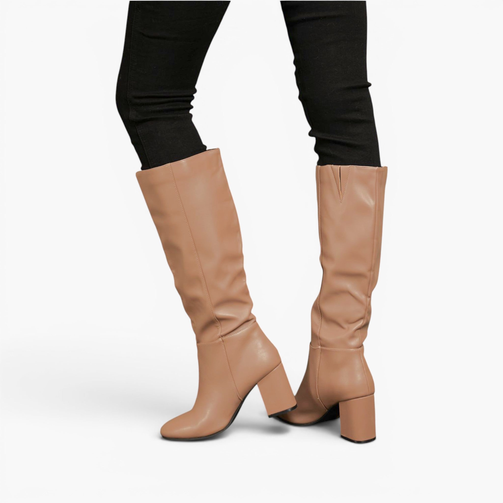 A pair of knee-high taupe leather boots with block heels, shown on a model wearing black skinny pants against a plain white studio background.