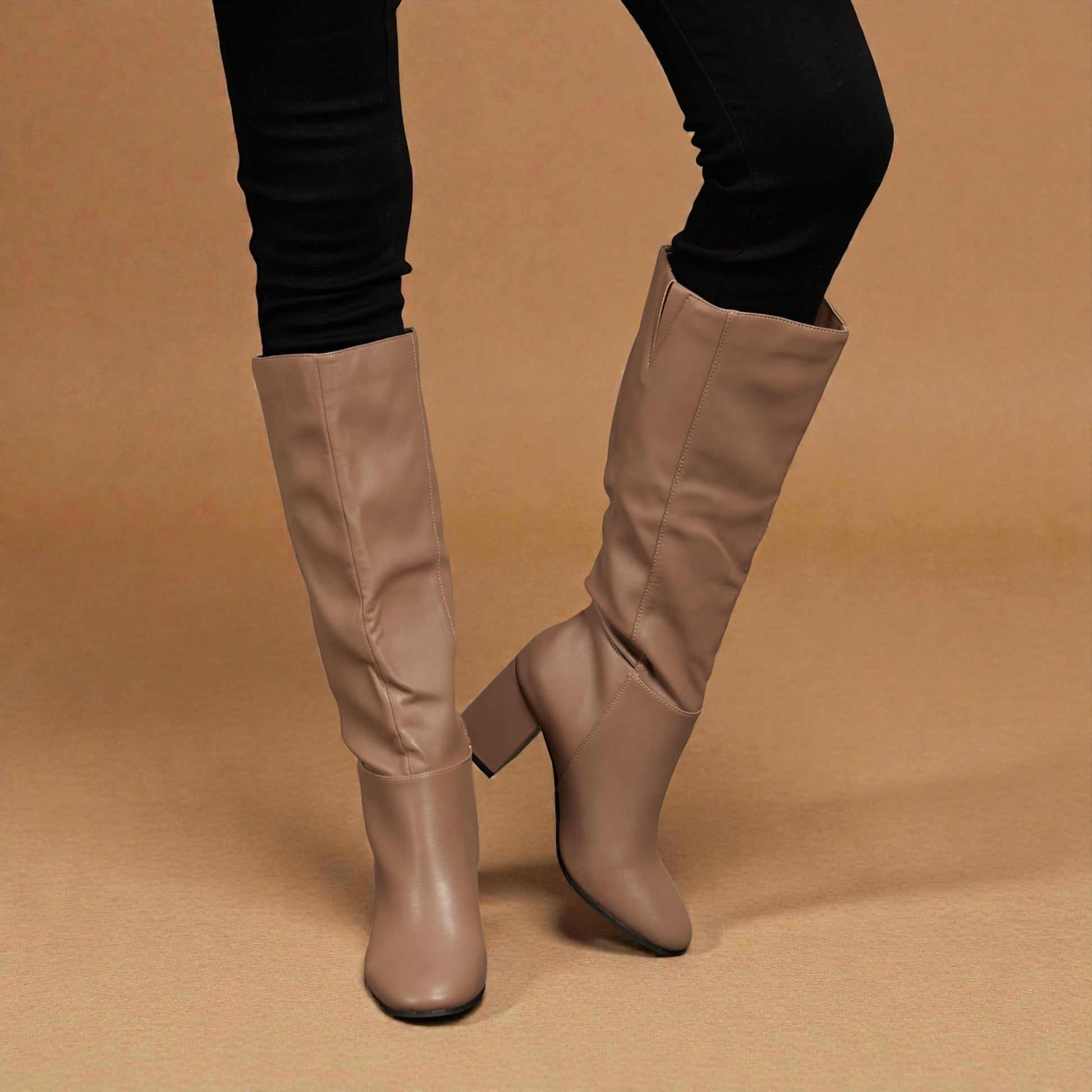 Beige knee-high boots worn with black pants on a brown background