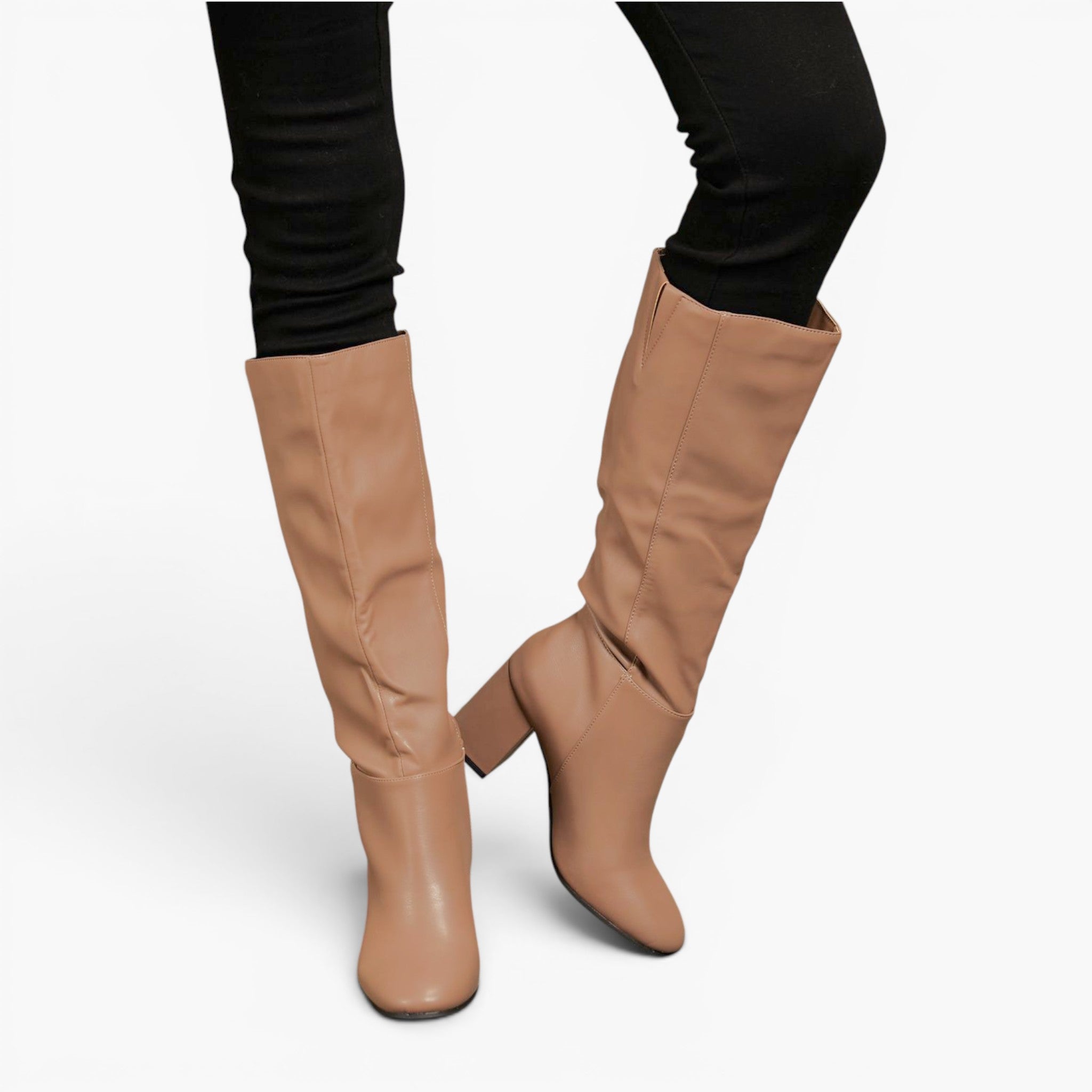 A pair of knee-high tan boots with a block heel, worn with black skinny pants against a light gray studio background.