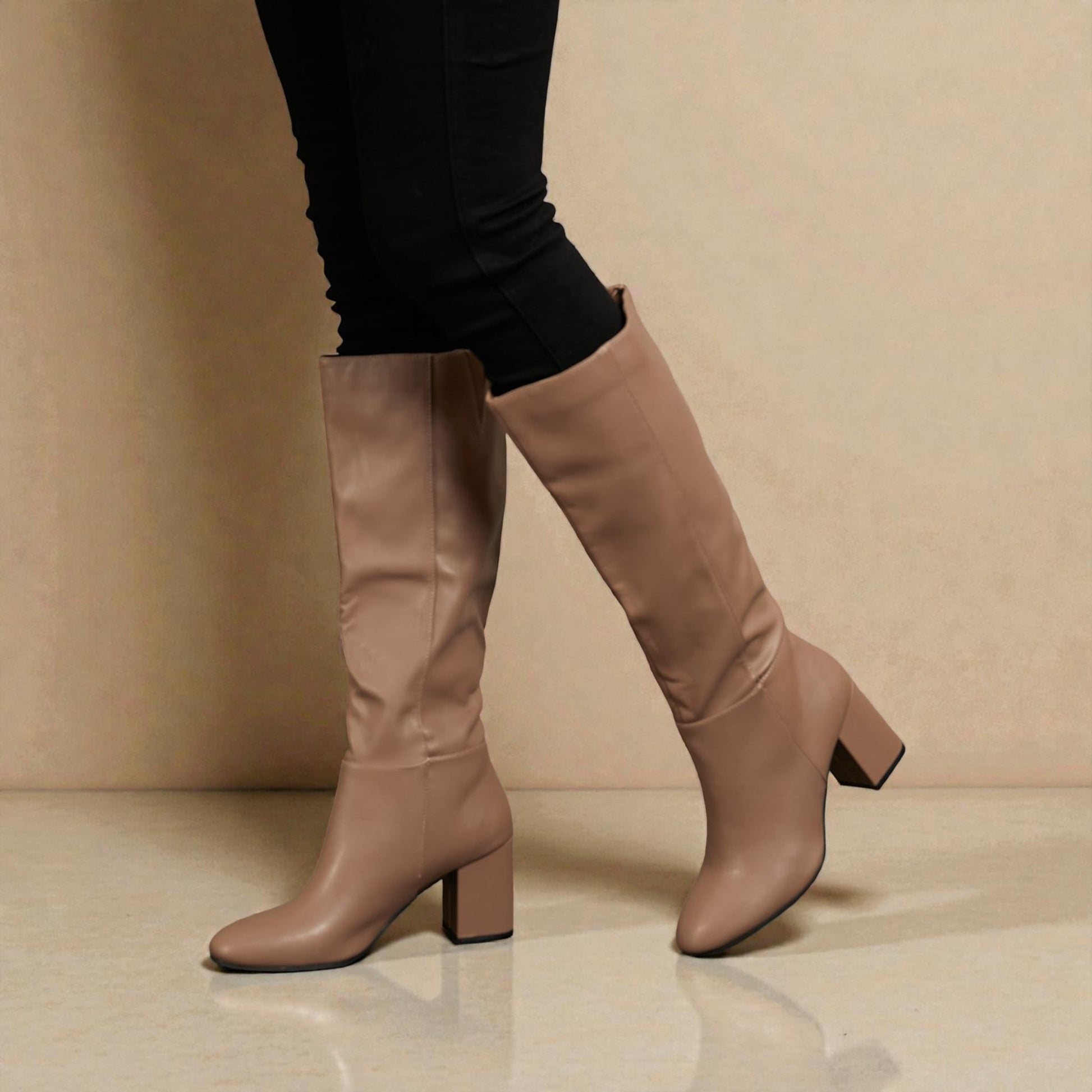 Beige knee-high boots worn with black leggings on a beige background
