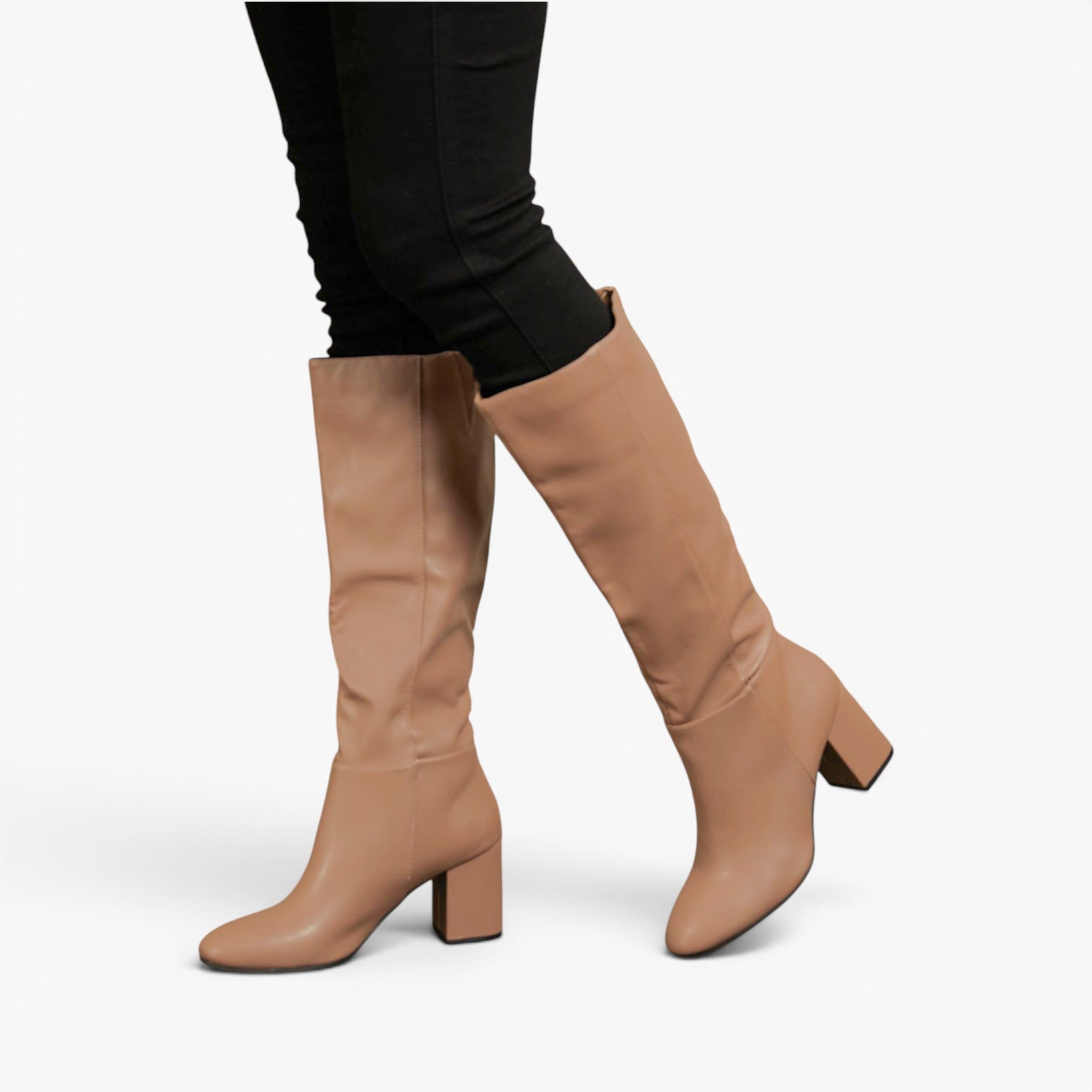 A pair of knee-high tan leather boots with a block heel, shown on a model wearing black pants against a light gray background.