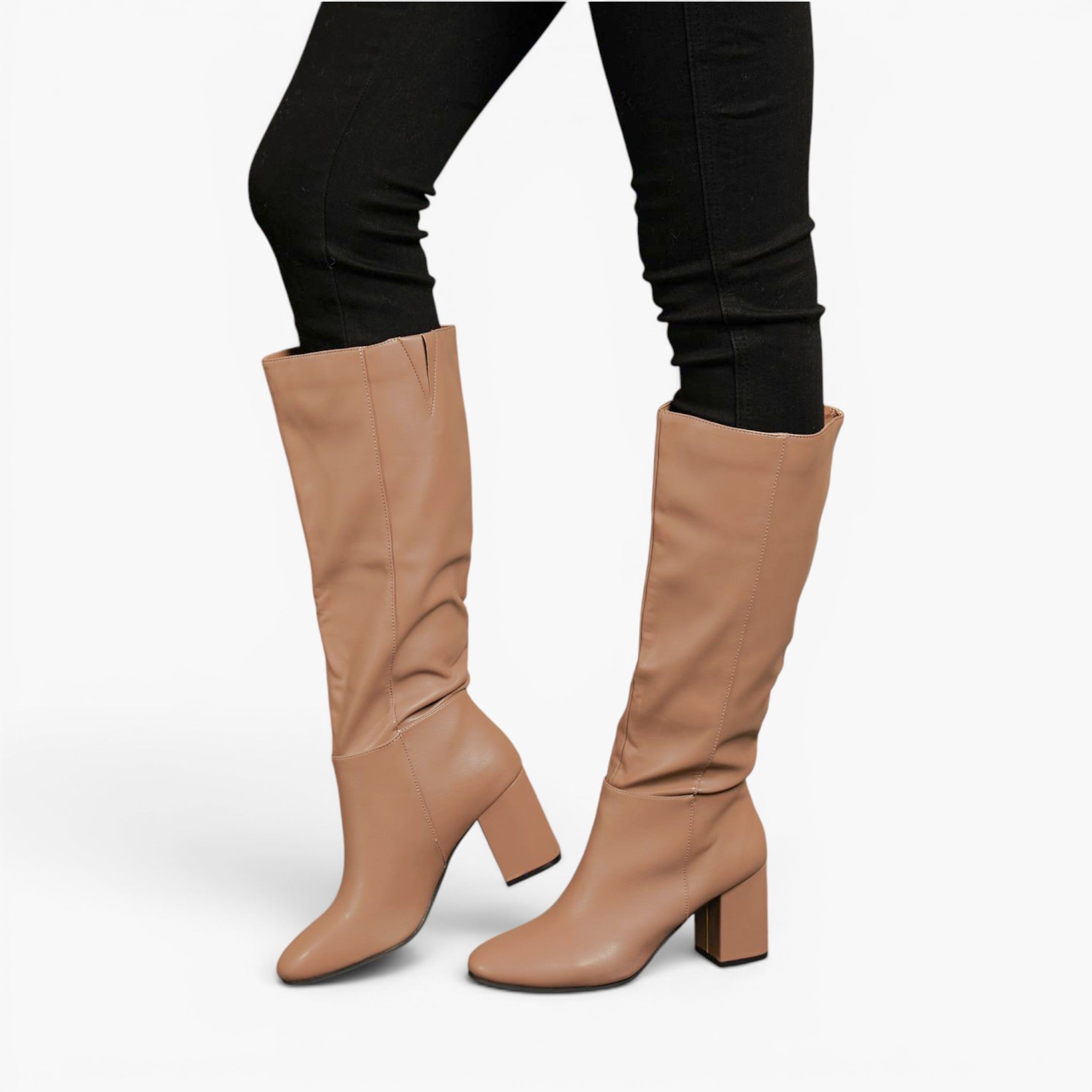 A pair of knee-high slouchy boots in a tan color, worn with black skinny pants against a light gray background.