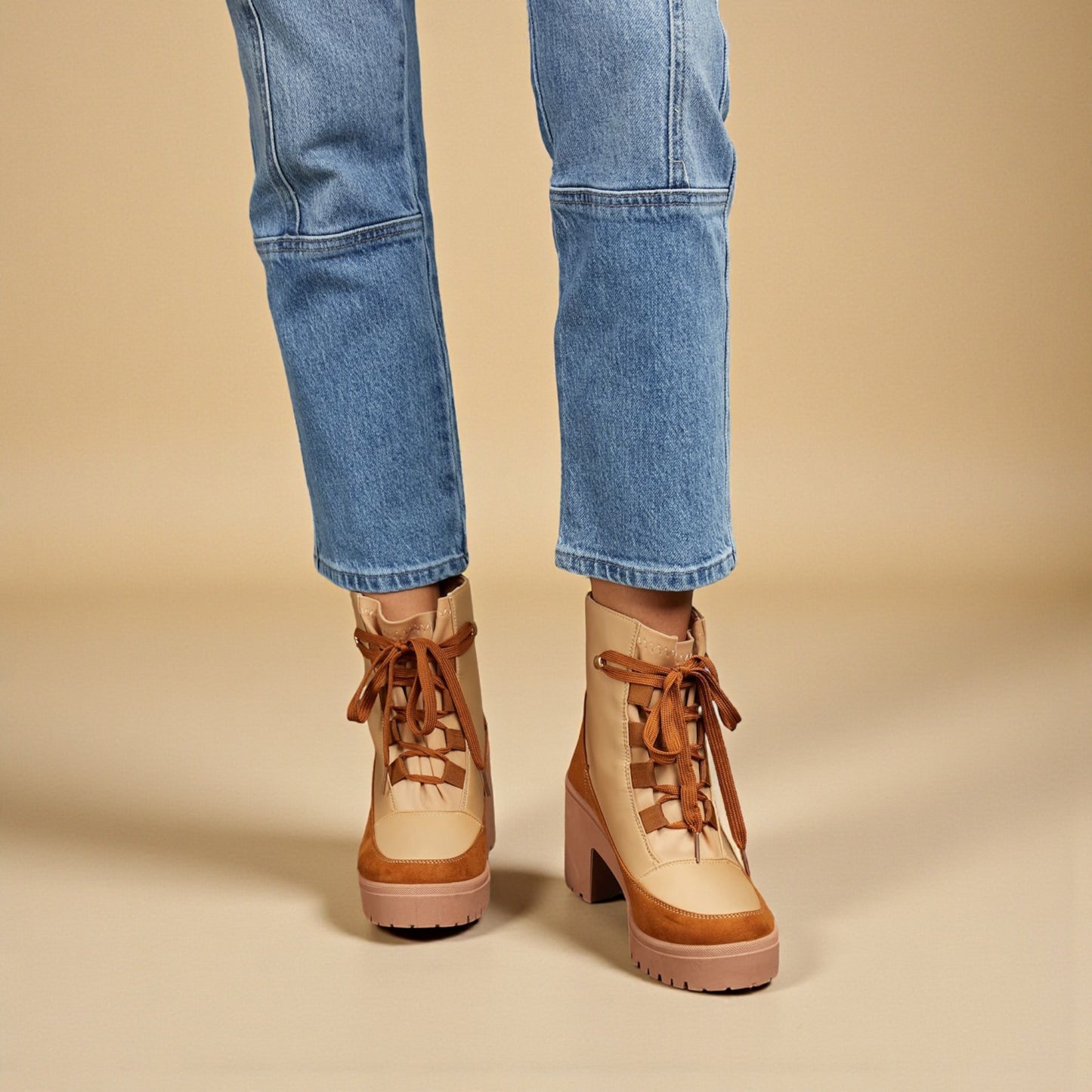 Tan platform boots with brown laces worn with blue jeans on a beige background