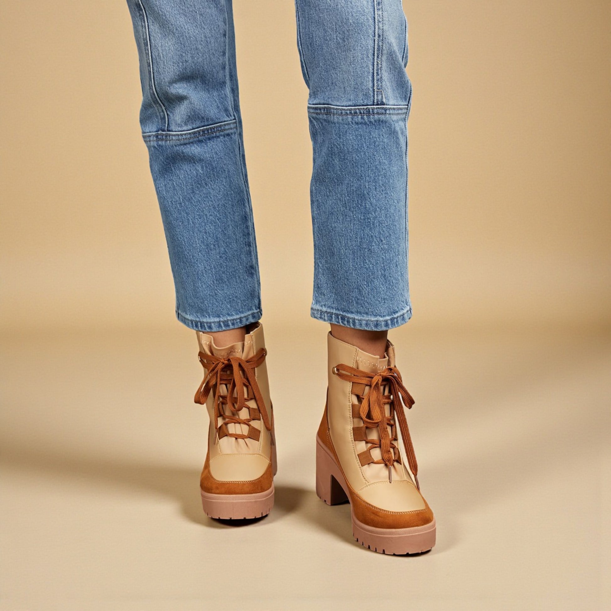 Tan platform boots with brown laces worn with blue jeans on a beige background