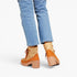 A person wearing light blue cropped jeans and orange-brown platform ankle boots with beige heels, shown from the back against a plain light gray studio background.