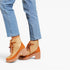 A pair of women's ankle boots in tan and light brown suede, styled with light-wash blue jeans against a plain white background.
