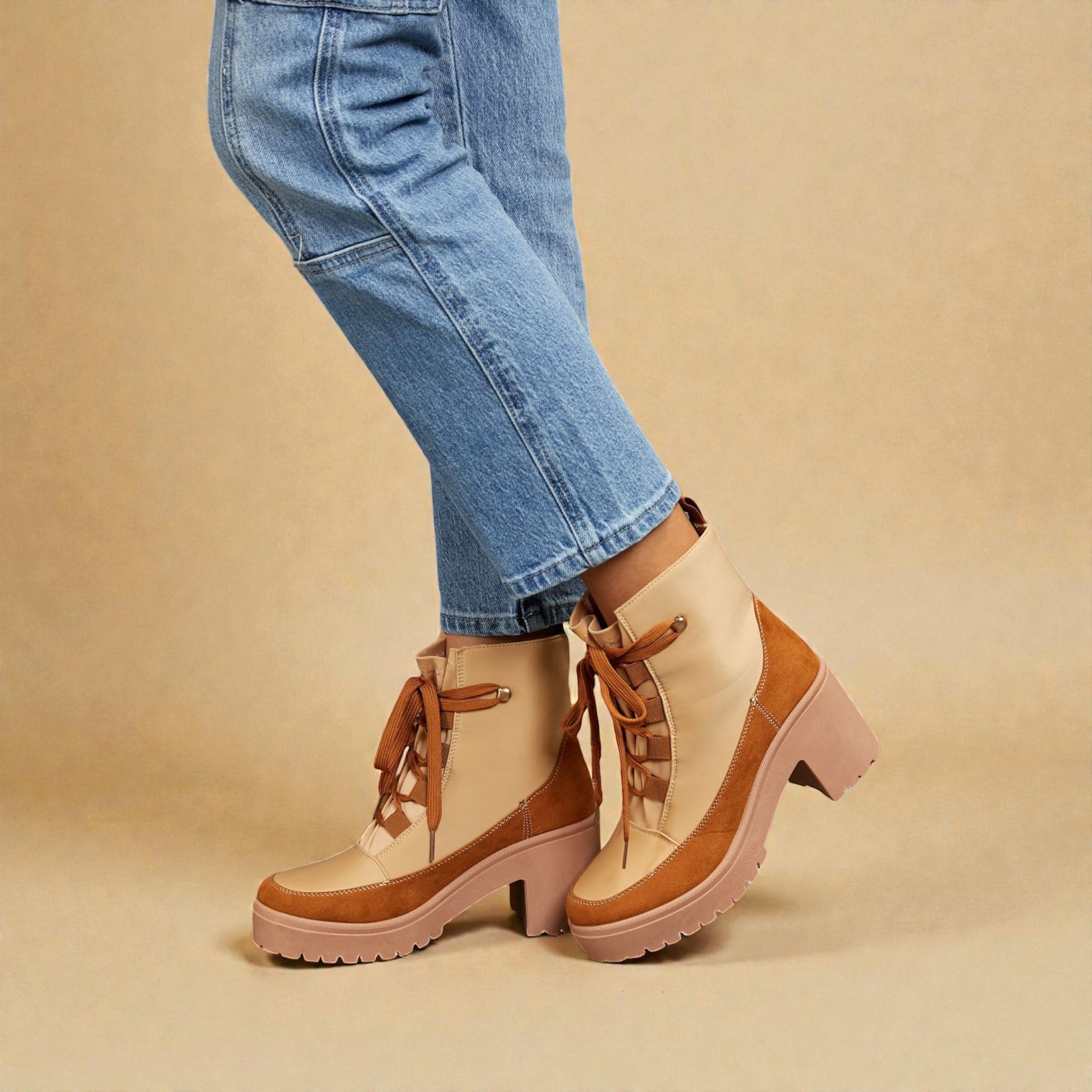 Tan and brown chunky-heeled boots worn with blue jeans on a beige background