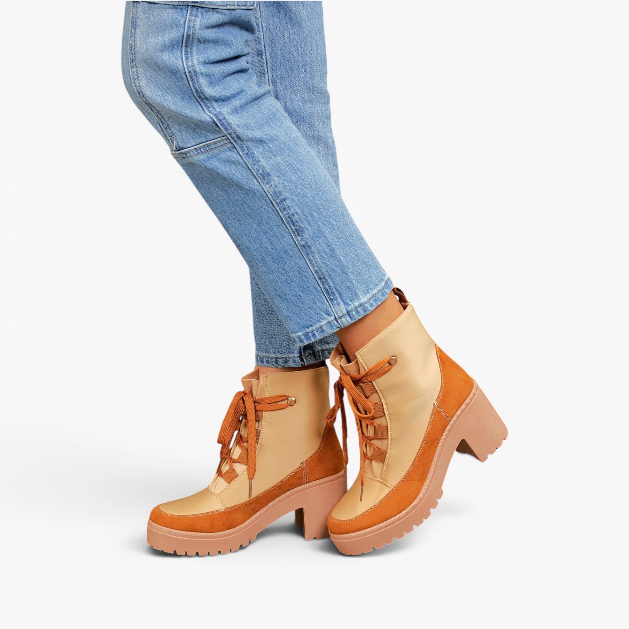 A person wearing light blue jeans and tan and beige lace-up ankle boots with chunky brown heels, shown against a plain light gray studio background.