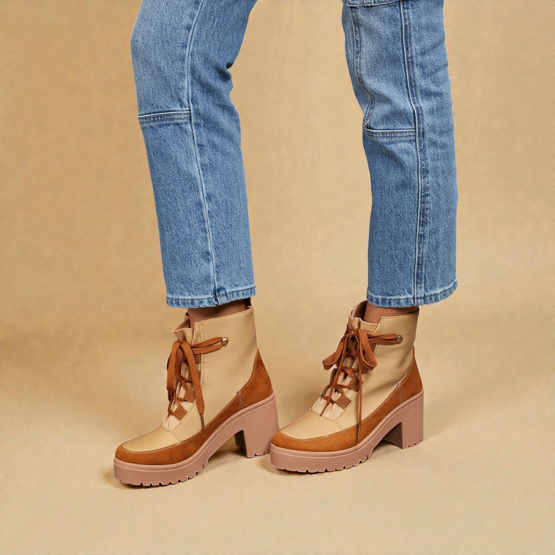 Brown lace-up boots worn with blue jeans on a beige background