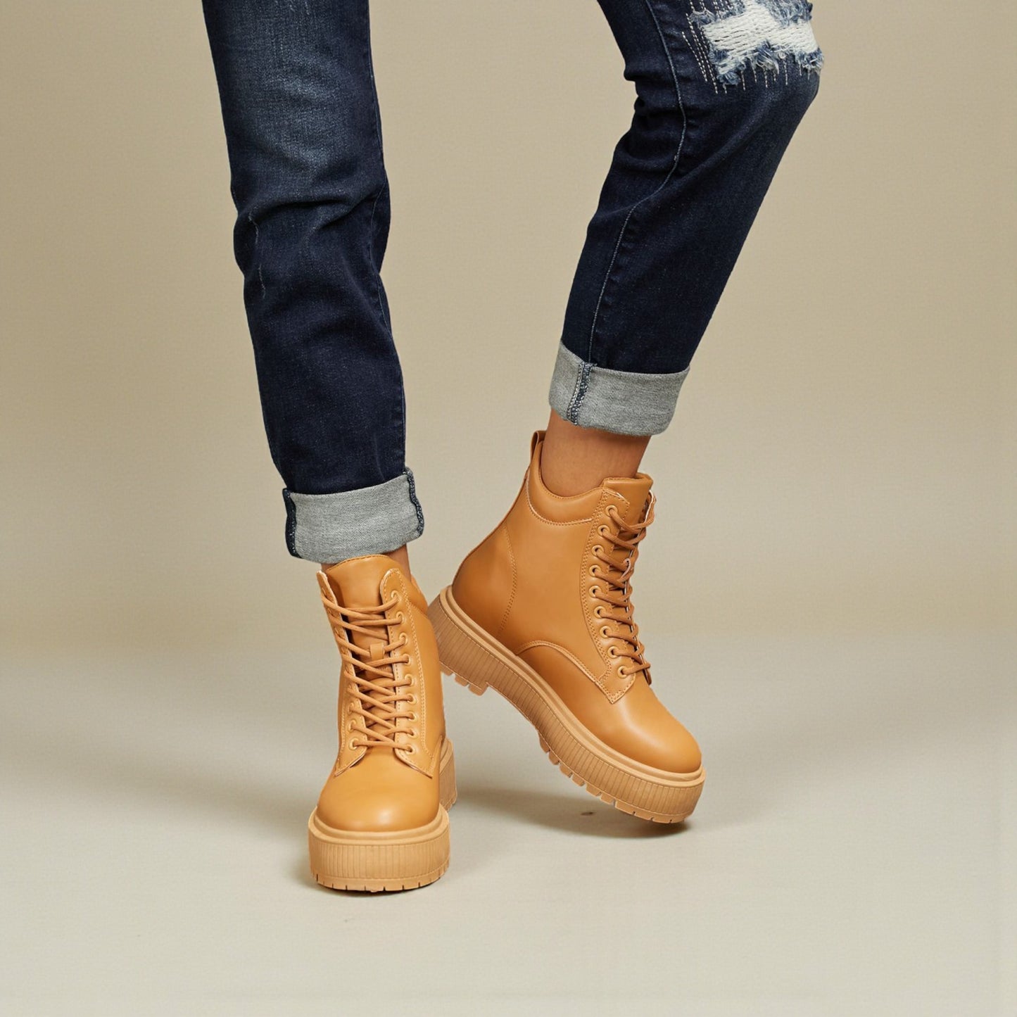 Tan leather boots worn with rolled-up jeans on a neutral background