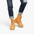 A person wearing tan lace-up platform ankle boots with dark blue cuffed jeans, shown from the calves down on a light gray studio background.