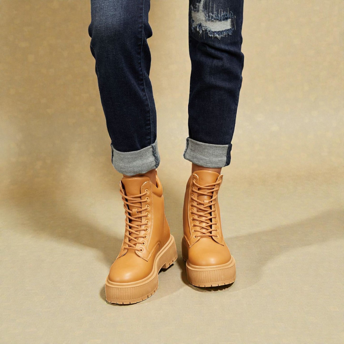 Tan combat boots worn with rolled-up jeans on a beige background