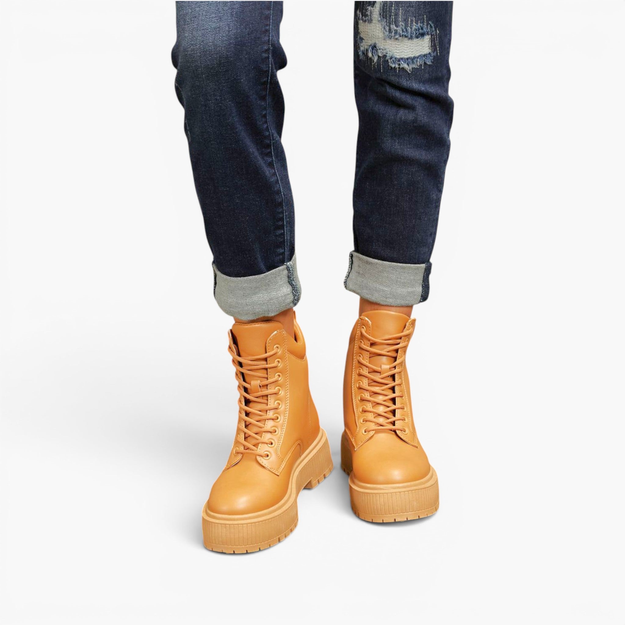 A person wearing dark blue cuffed jeans and tan lace-up platform boots against a clean white background.