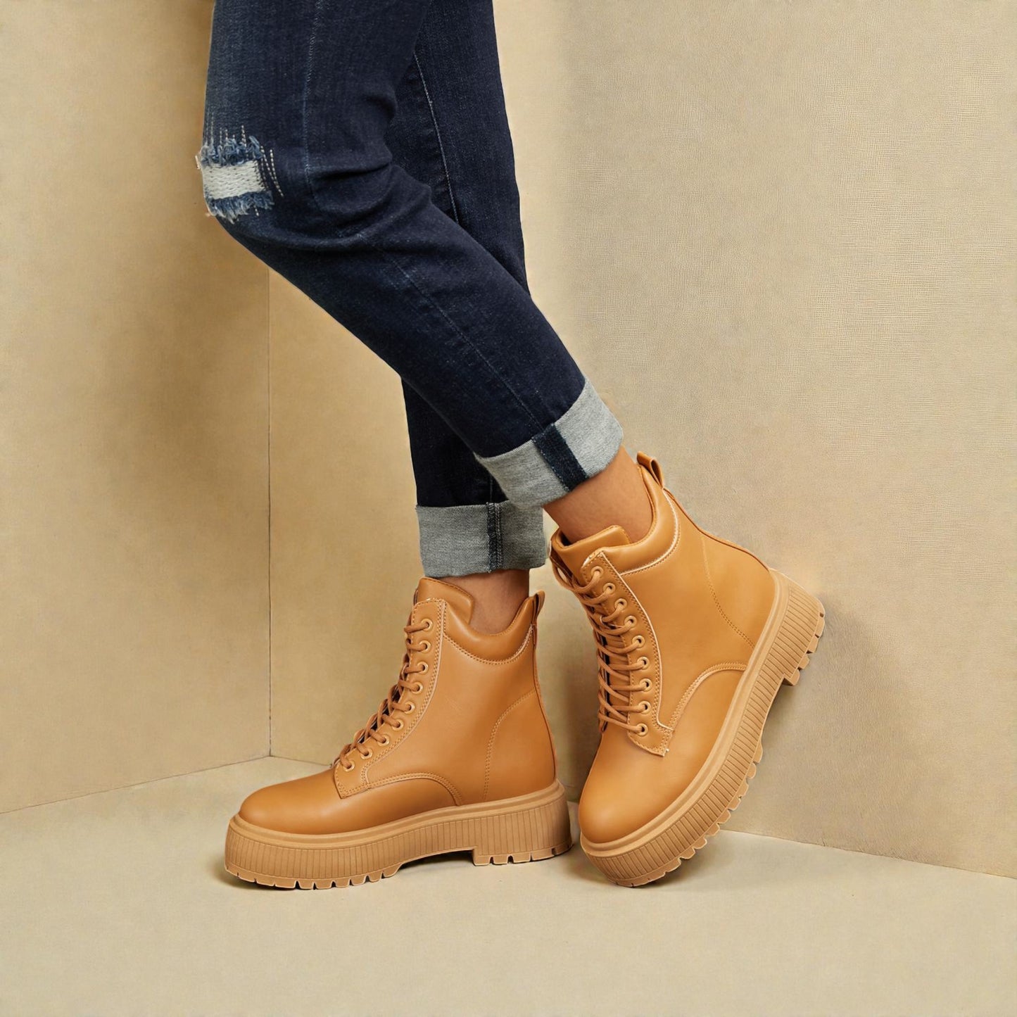 Tan boots worn with rolled-up jeans against a beige background
