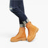 A person wearing tan lace-up platform ankle boots with dark blue ripped jeans, shown from the calves down against a clean white studio background.