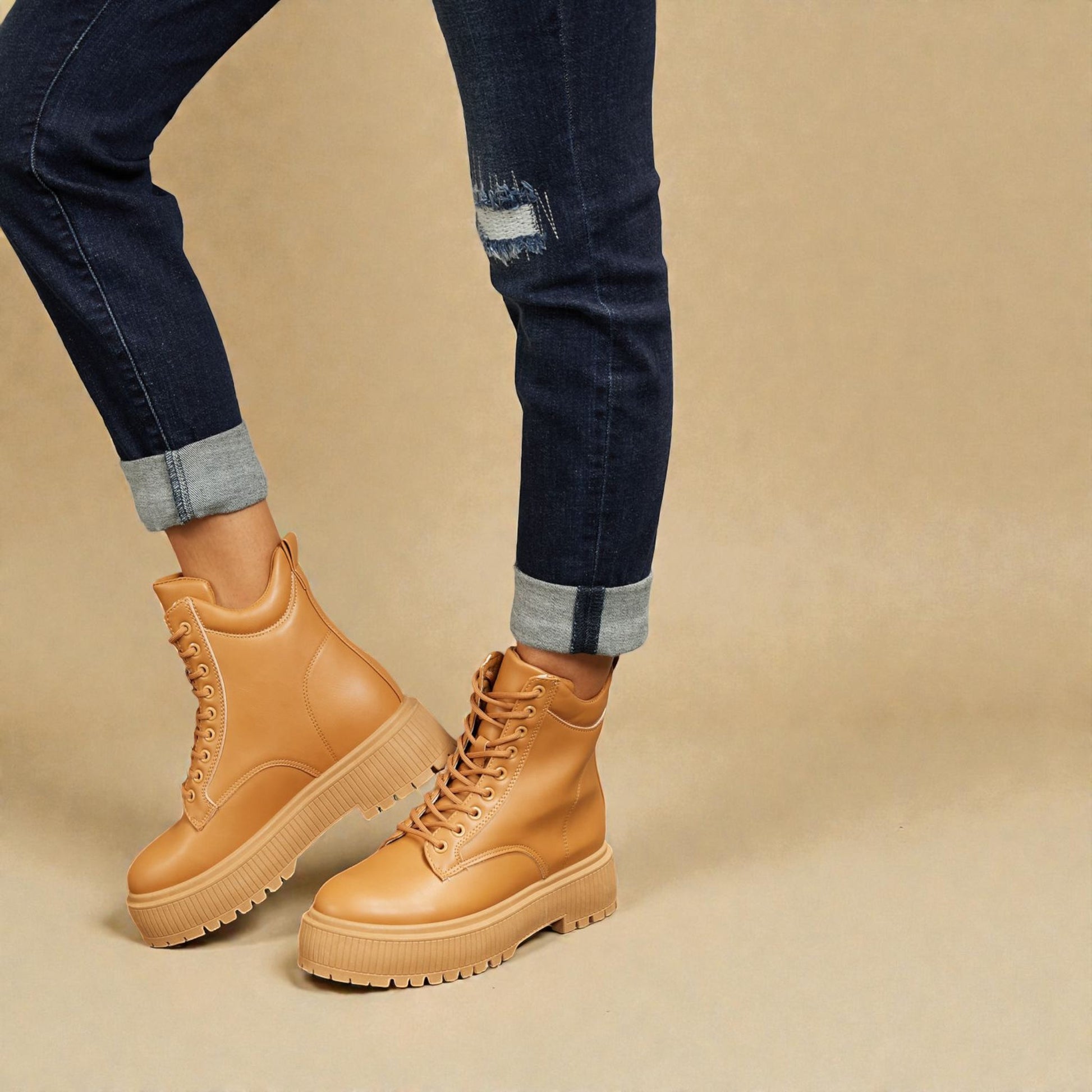 Tan boots worn with rolled-up jeans on a beige background