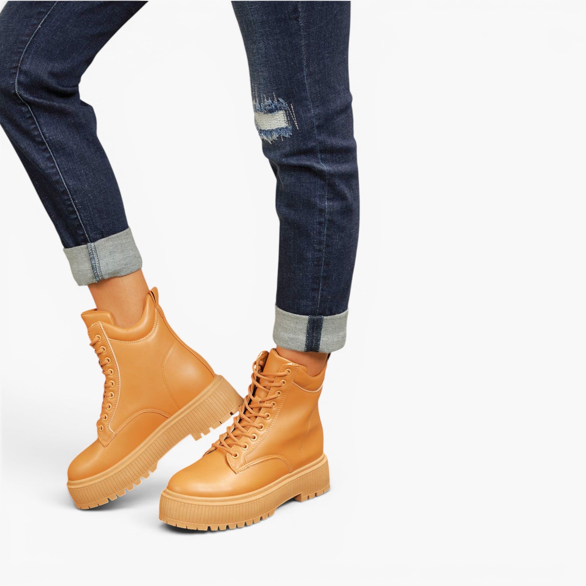 A pair of tan lace-up platform combat boots worn with dark blue cuffed jeans, shown from the knees down on a light gray studio background.