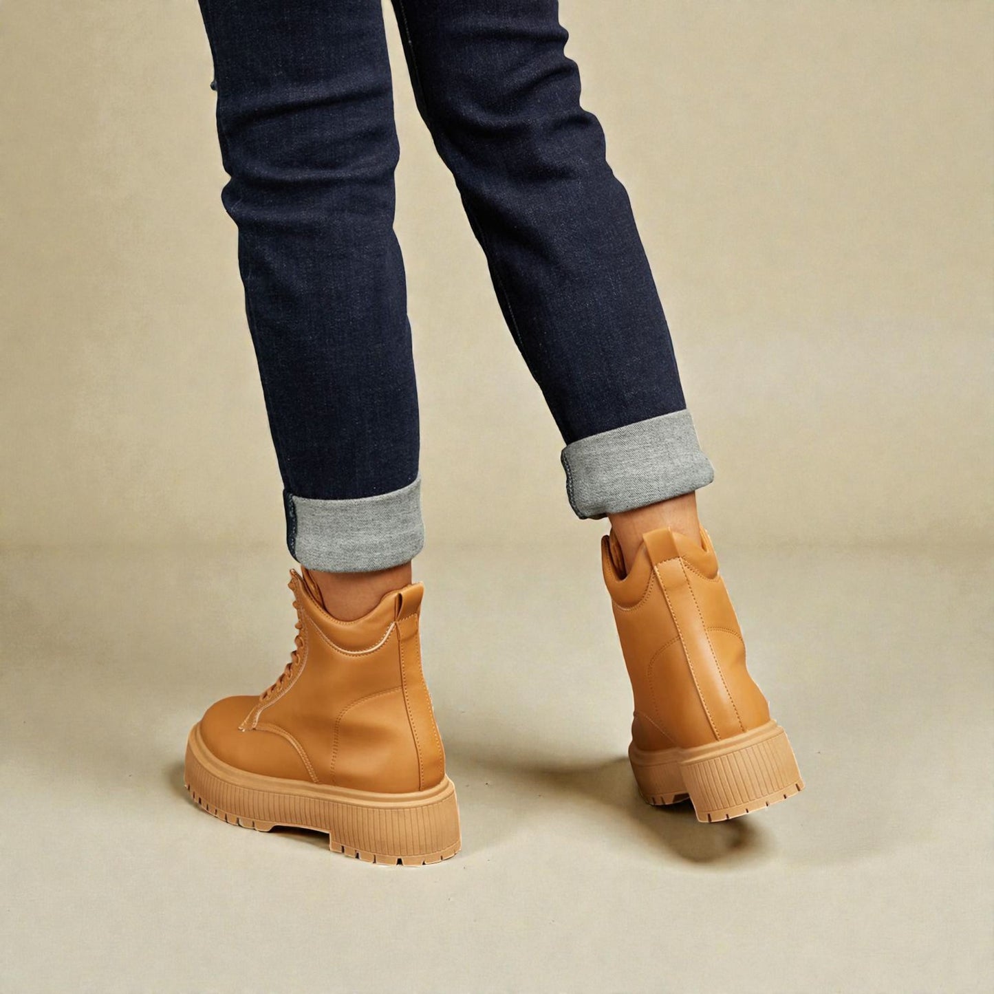 Tan boots worn with rolled-up jeans on a beige background