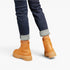 A person wearing dark blue cuffed jeans and tan lace-up ankle boots, shown from the back against a clean white studio background.