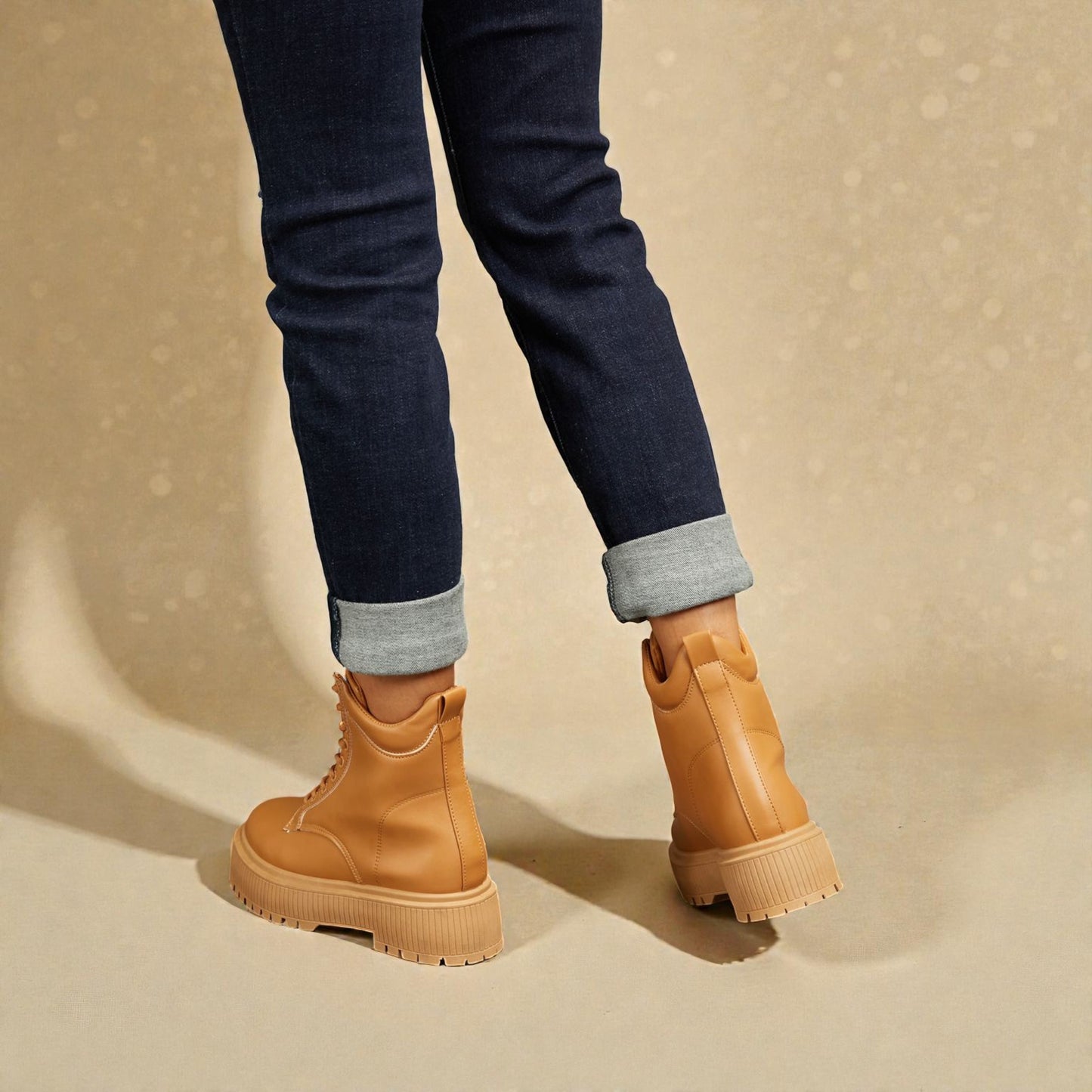 Tan boots worn with rolled-up jeans on a beige background