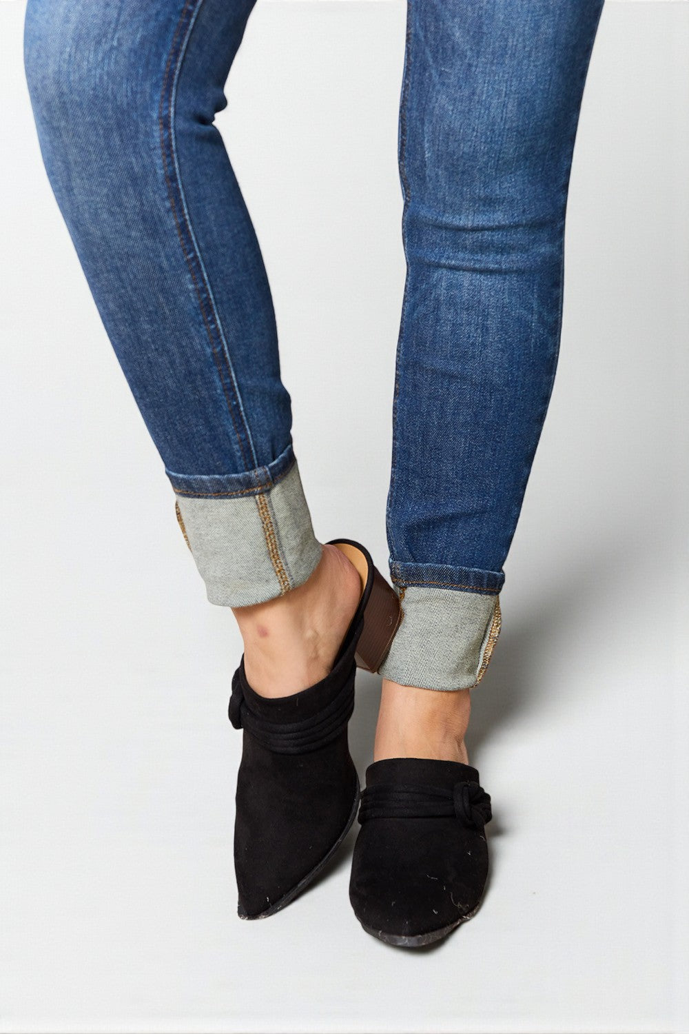 Close-up of blue jeans with rolled-up cuffs and black suede shoes on a light gray background