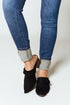 Person wearing blue jeans with rolled-up cuffs and black suede shoes on a white background